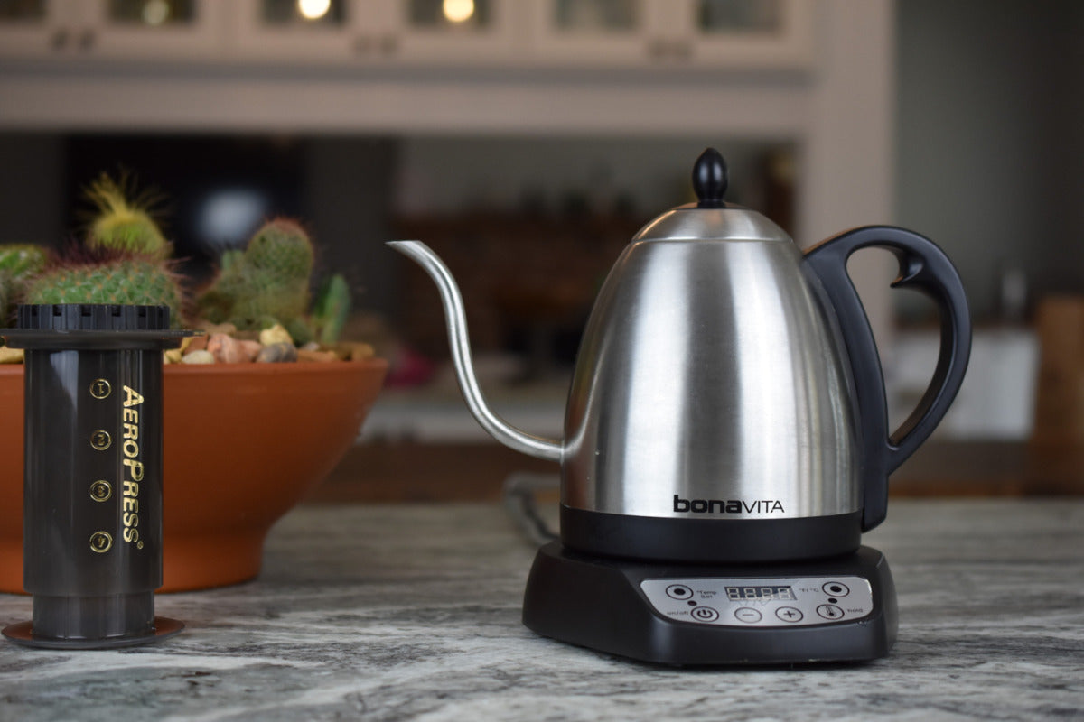 Stainless steel electric kettle with digital display on a kitchen counter, accompanied by an Aeropress coffee maker.