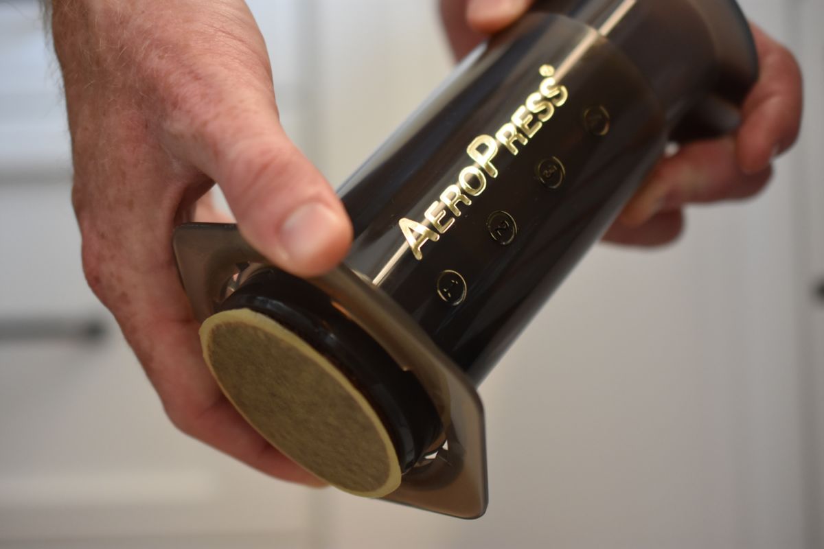 A person holding an AeroPress coffee maker against a neutral background