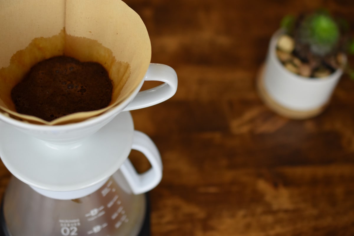 Coffee filter with coffee grounds in a white mug on a wooden surface