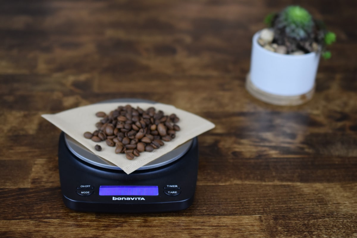 Coffee beans measured on a digital Bonavita scale, placed on a piece of folded paper.