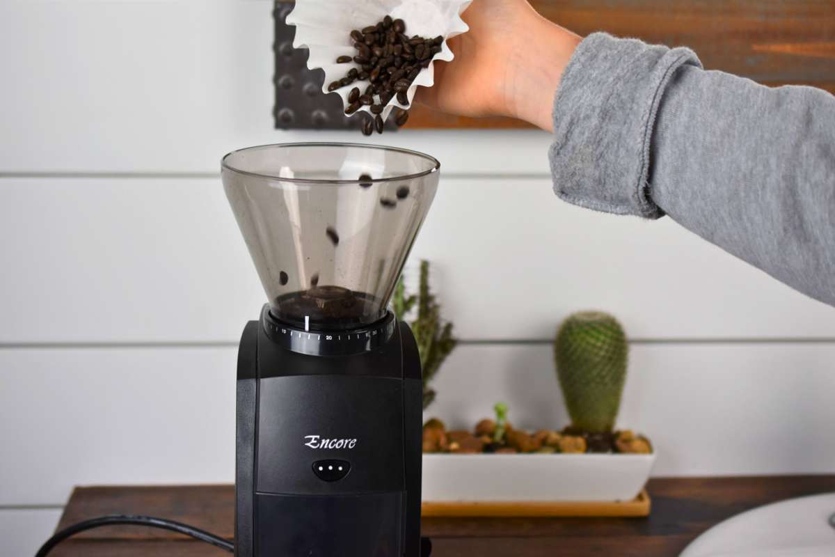 Person loading coffee beans into a coffee grinder with a blurred background
