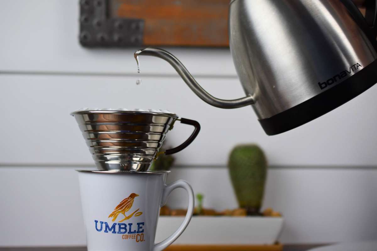 Coffee being poured from a kettle into a Umble coffee cup with a filter.