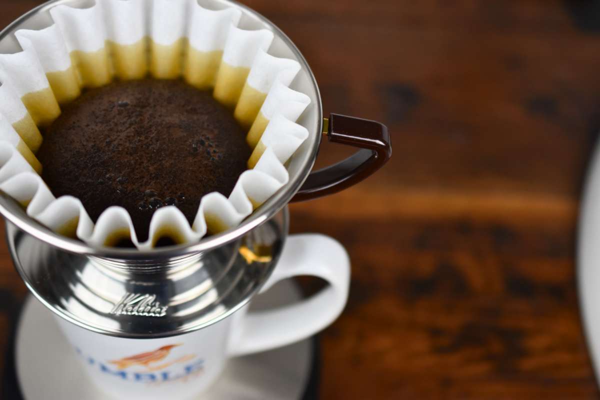 Coffee filter with ground coffee in a metal dripper on a blurred background