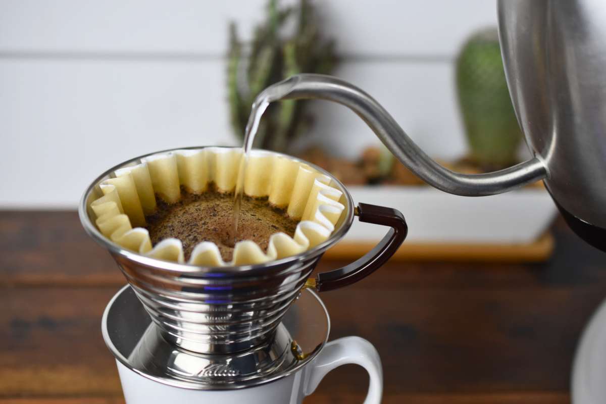 Coffee being poured into a filter with a metal kettle on a wooden surface.