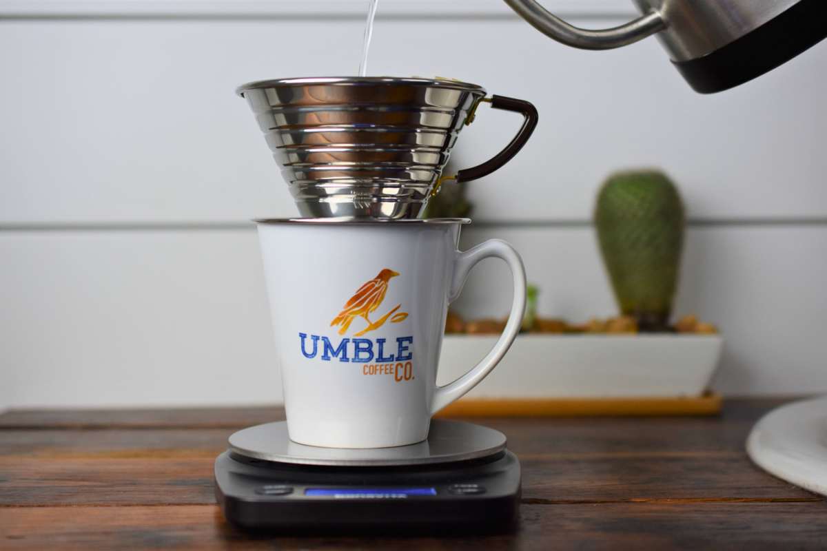 Coffee being poured into a white mug with 'Umble Coffee Co.' logo on a digital scale.