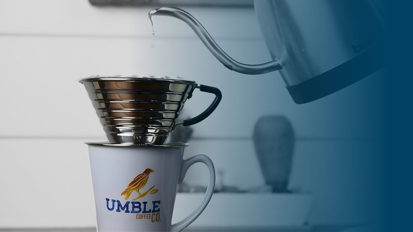 Gooseneck kettle pouring water into a stainless steel Kalita Wave dripper set on a white Umble Coffee Co. mug.
