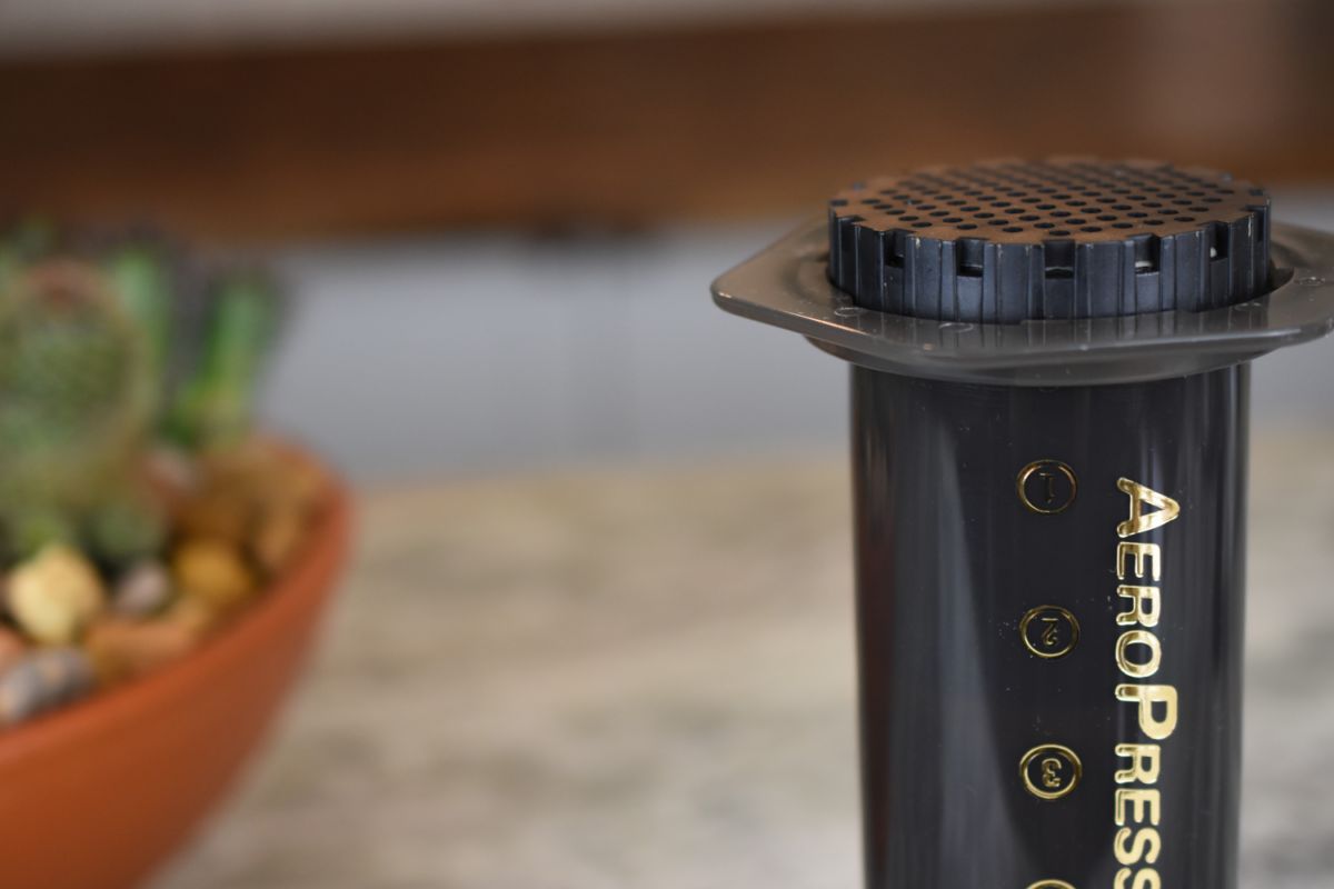 AeroPress coffee maker on a blurred background with a plant