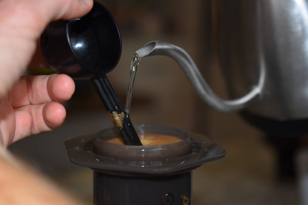 Hand pouring liquid from a black container into a brown device with a blurred background