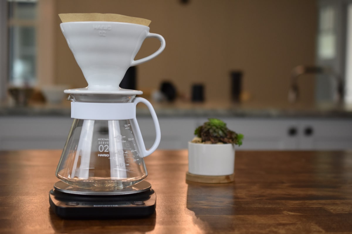 Hario V60 dripper with paper filter set on a glass carafe, placed on a digital scale.