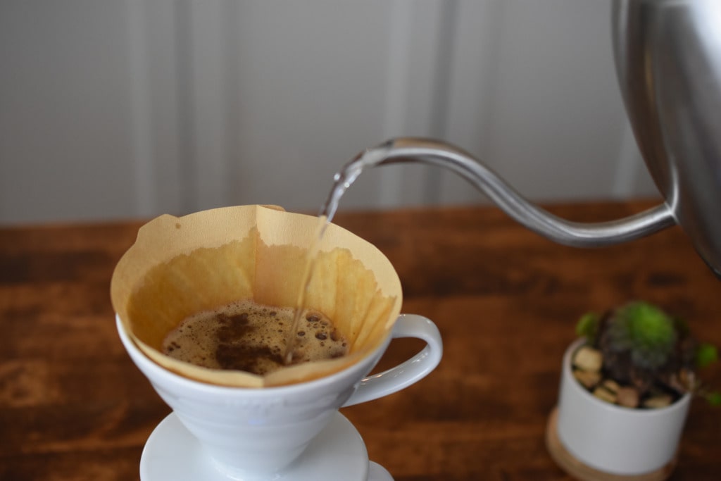 Close-up of hot water being poured over coffee grounds blooming inside a Hario V60 dripper.
