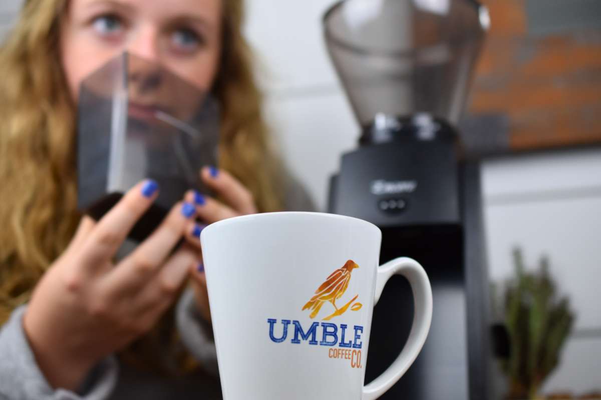 Person holding a box with a coffee grinder in the background, featuring an Umble Coffee mug.